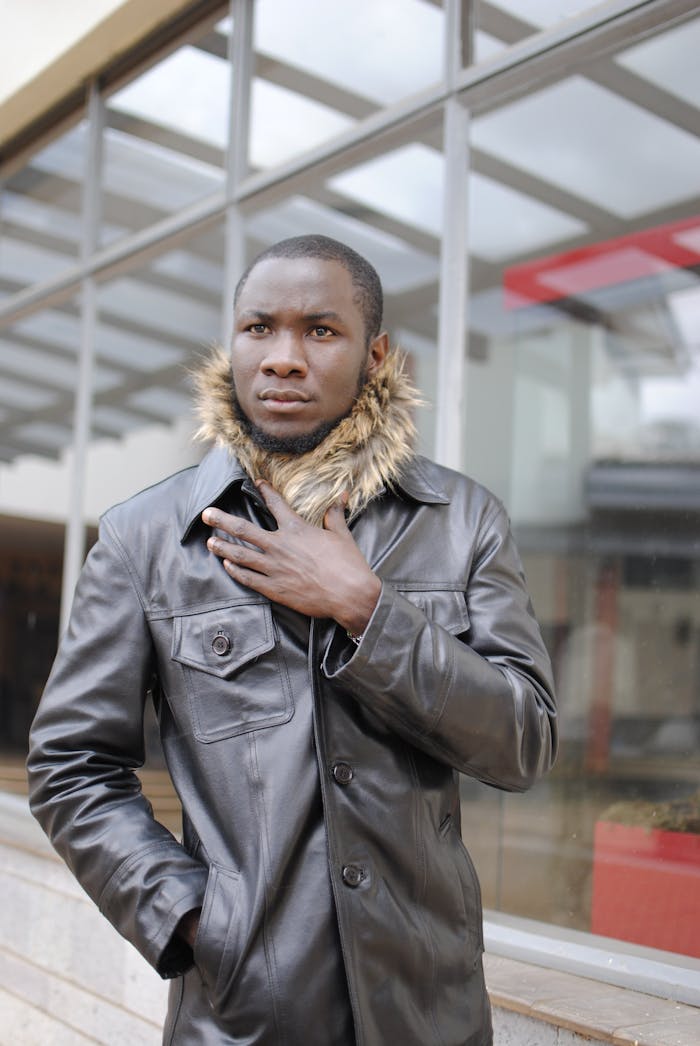 Stylish portrait of a male fashion model wearing a leather jacket with fur collar, outdoors.