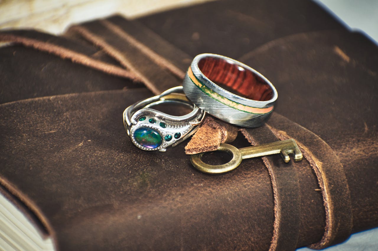 about-03 Close-up of exquisite rings on a leather journal with a vintage key, capturing elegance and craftsmanship.
