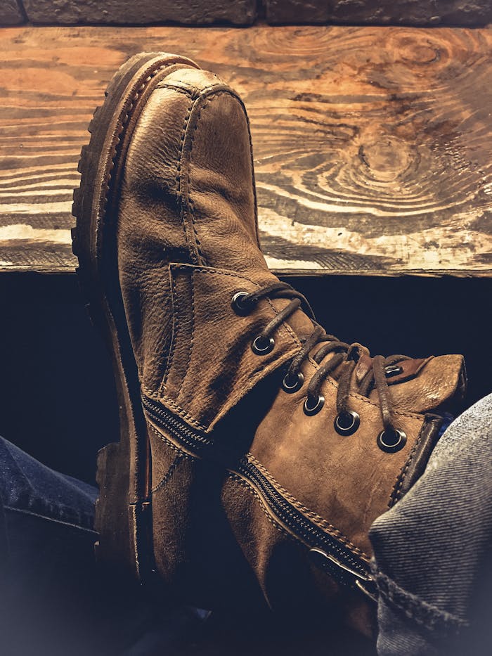 menu-03 A close-up view of rugged brown leather boots resting on a wooden surface, showcasing vintage fashion.