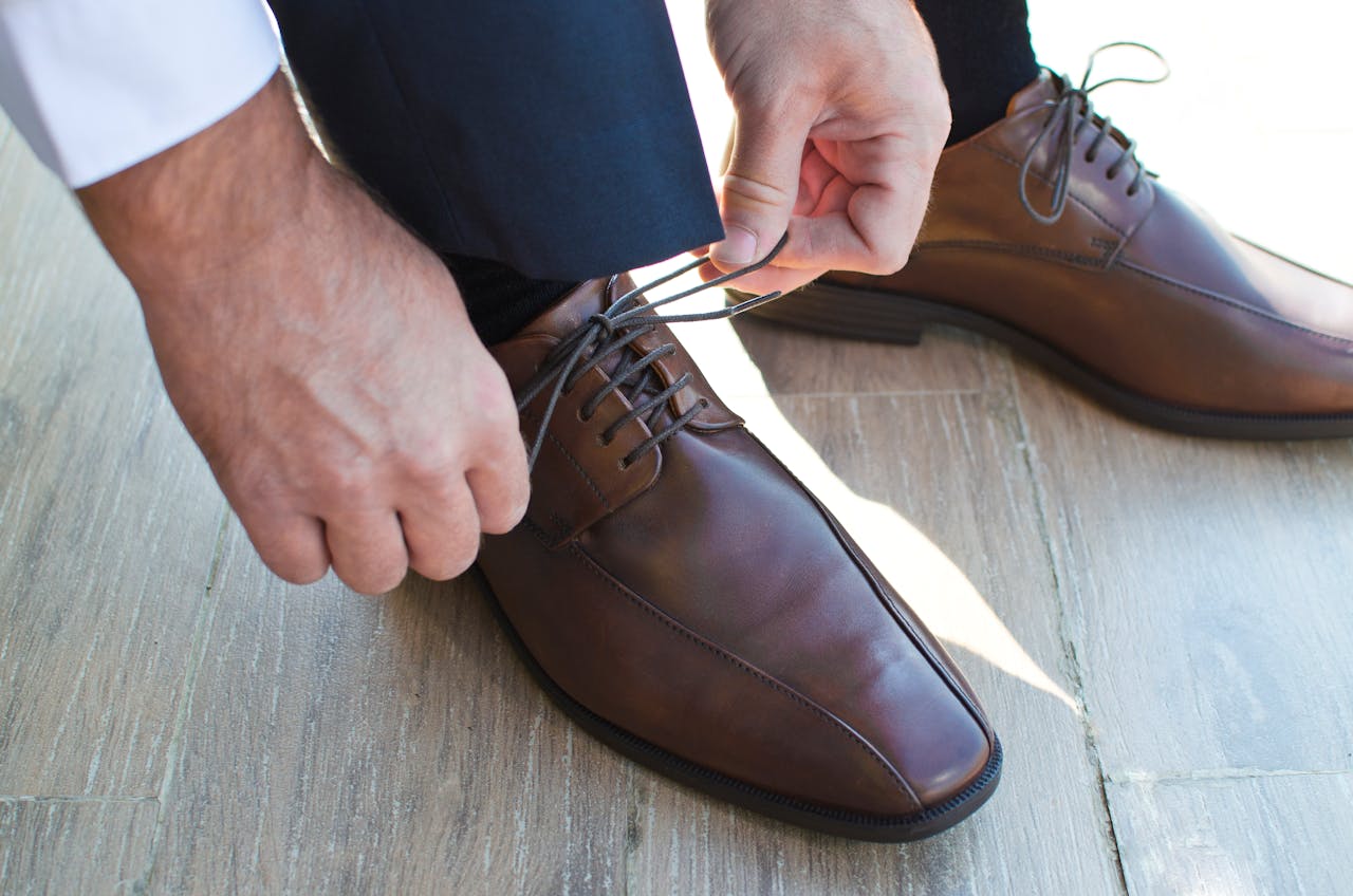 about-02 Close-up of a man tying elegant brown leather shoes on a wooden floor.
