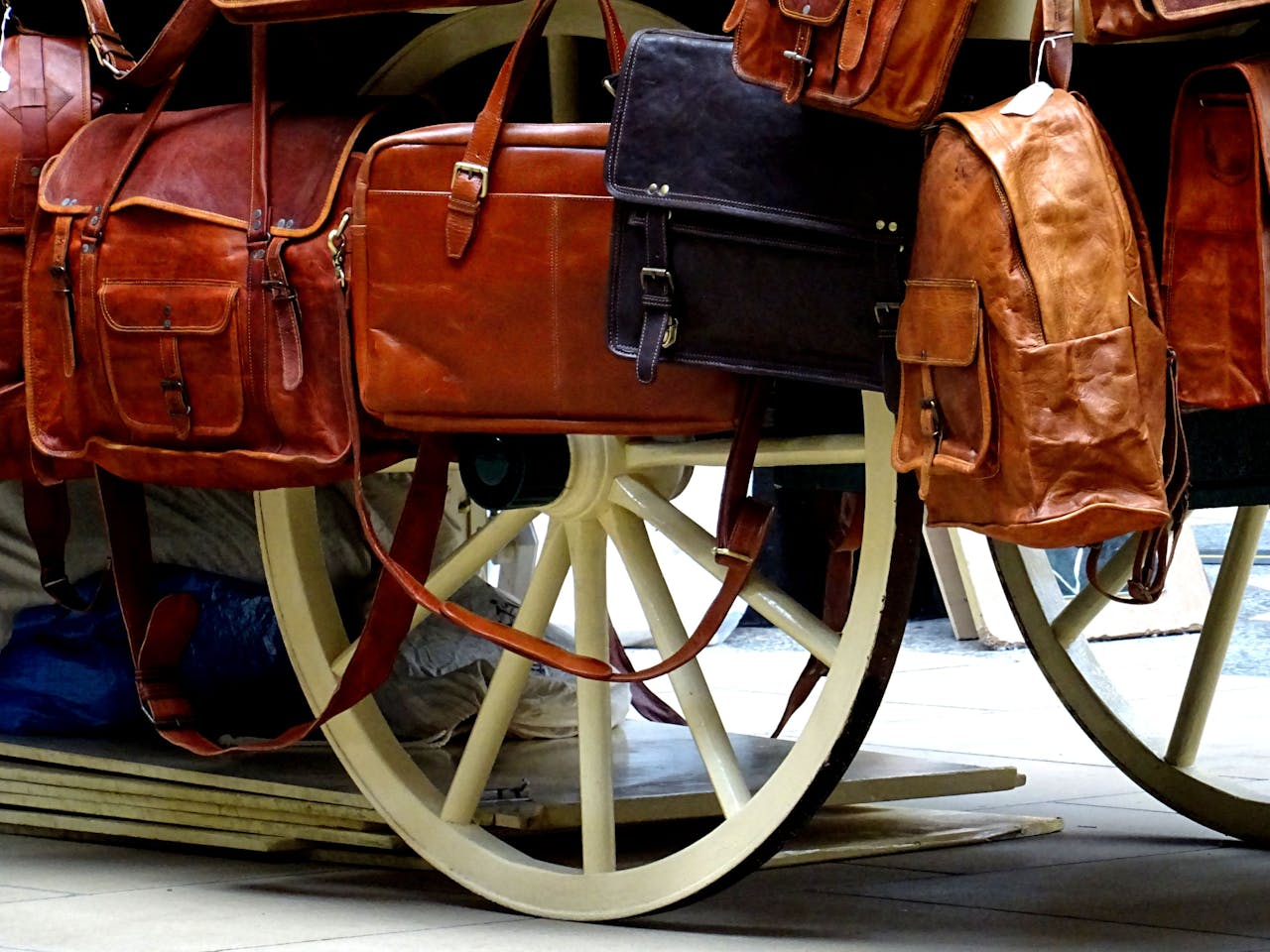 about-02 A variety of leather bags elegantly displayed on a classic wooden carriage wheel.