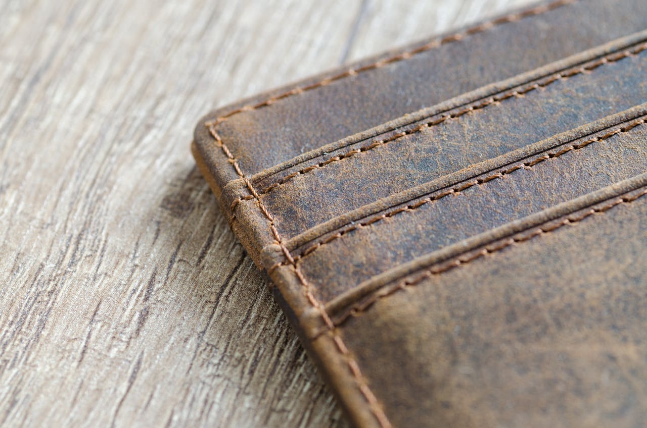 menu-02 Detailed shot of a brown leather wallet on a textured wooden surface, showcasing stitching.